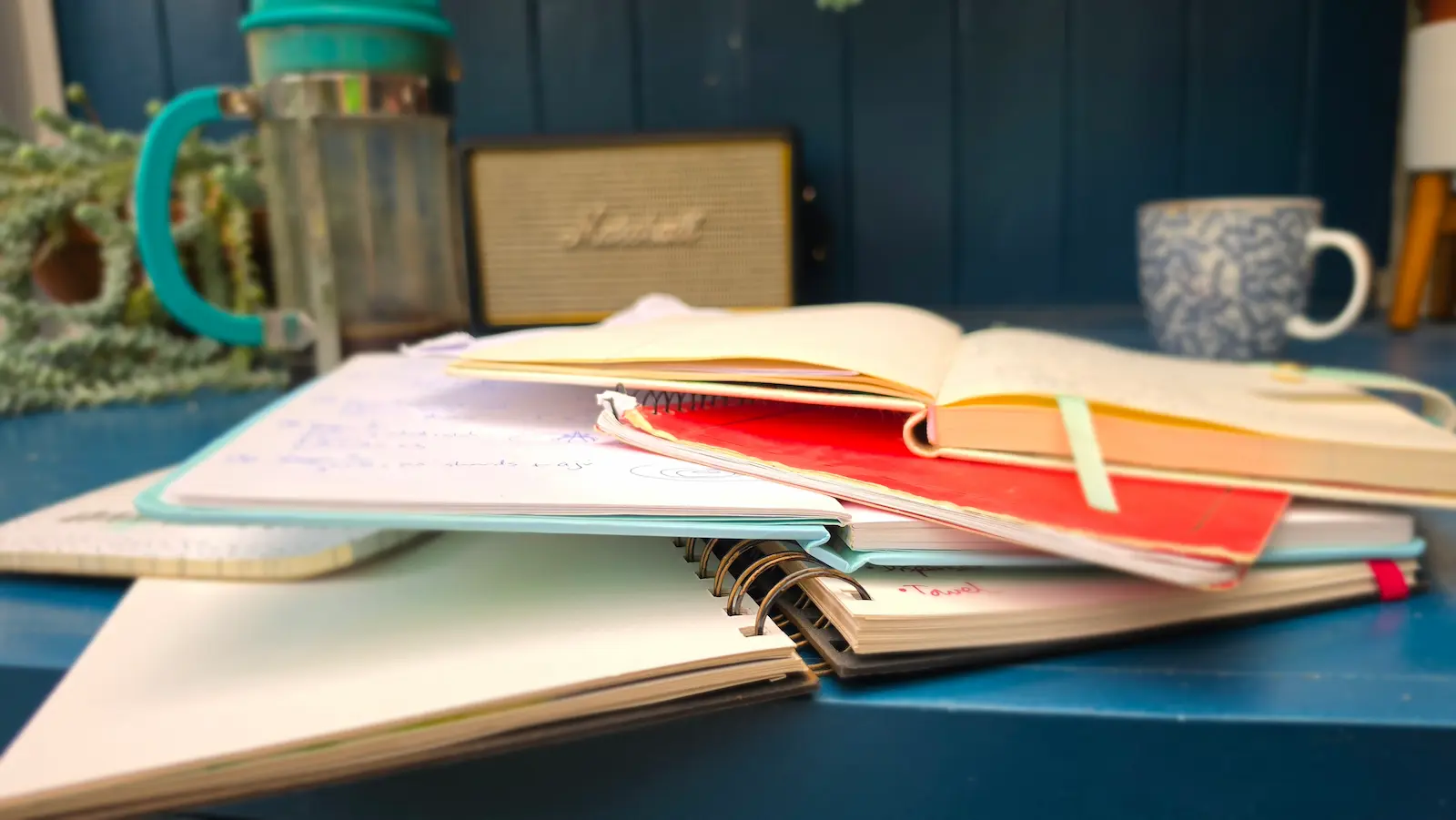 Pile of well-used notebooks stacked on a blue desk - ideas captured before they became projects