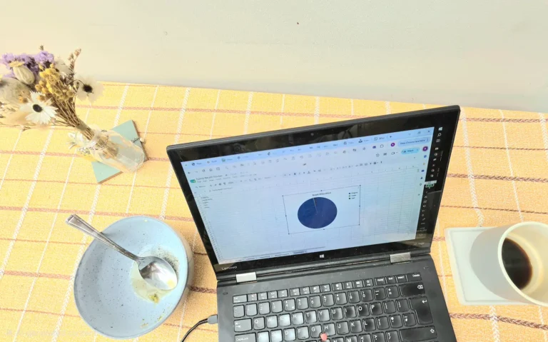 Laptop showing family net worth tracker spreadsheet with asset allocation chart, coffee and breakfast on kitchen table - family finances Google Sheets